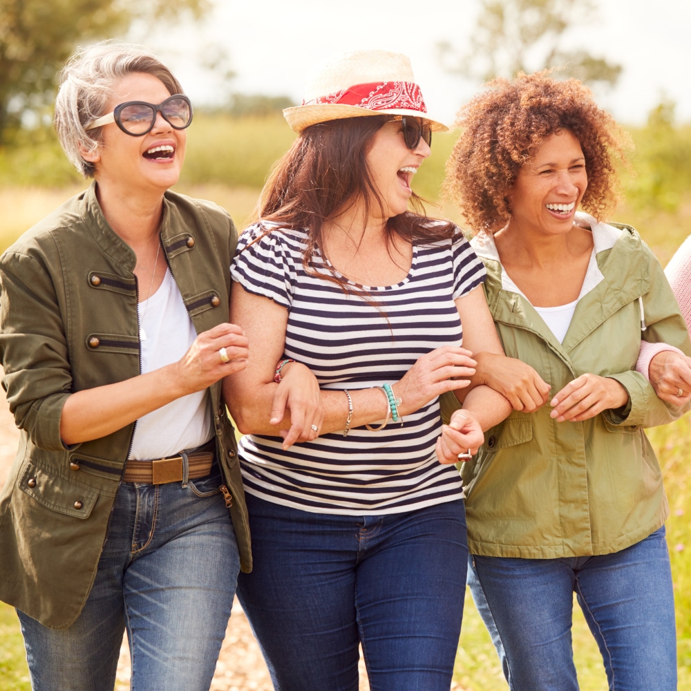 three women smile and link arms as they walk outside