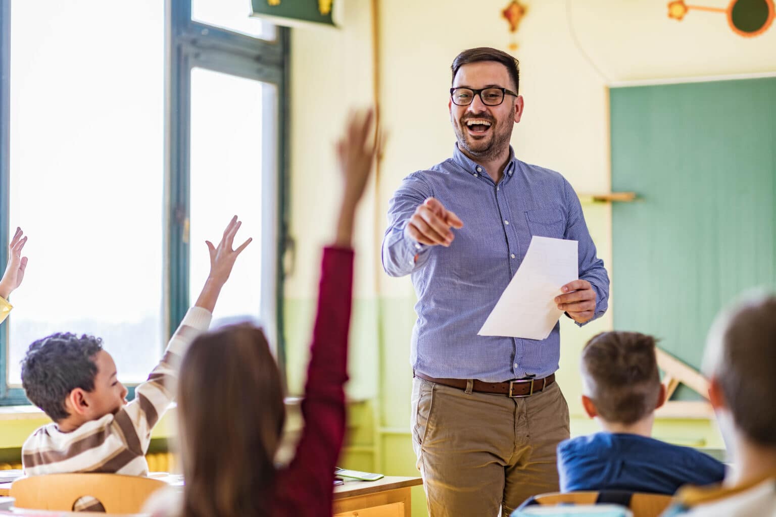 a teacher points at his students who raised their hands to answer the question in an elementary school class