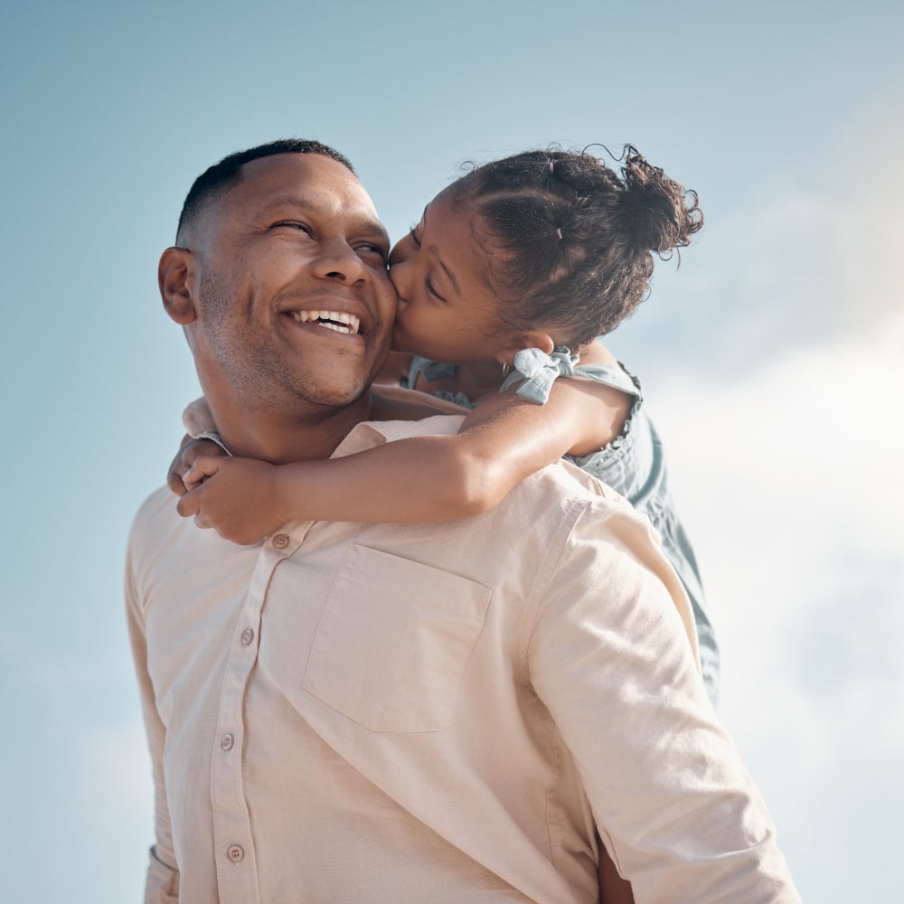 a young girl gets a piggyback ride from her father and kisses his cheek